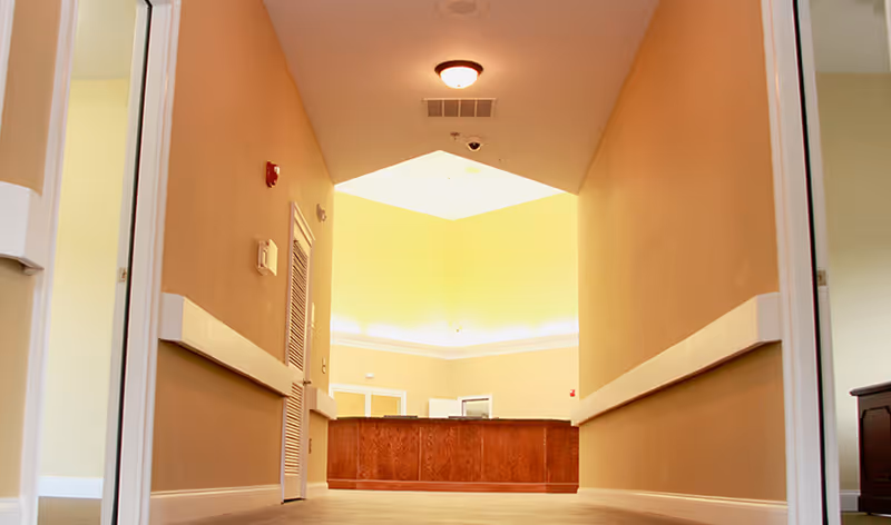 Low-angle view down a hallway toward a reception desk in a senior living facility lobby.