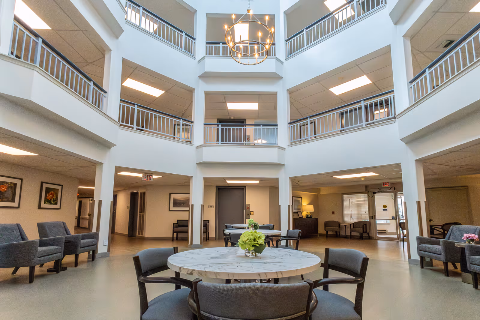 Atrium-style common area with a round table and chairs, lounge seating, multi-level balconies, and a hanging chandelier.