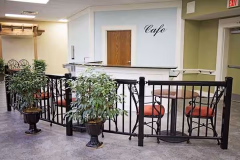 Indoor cafe area with railing, potted plants, and red-cushioned chairs.