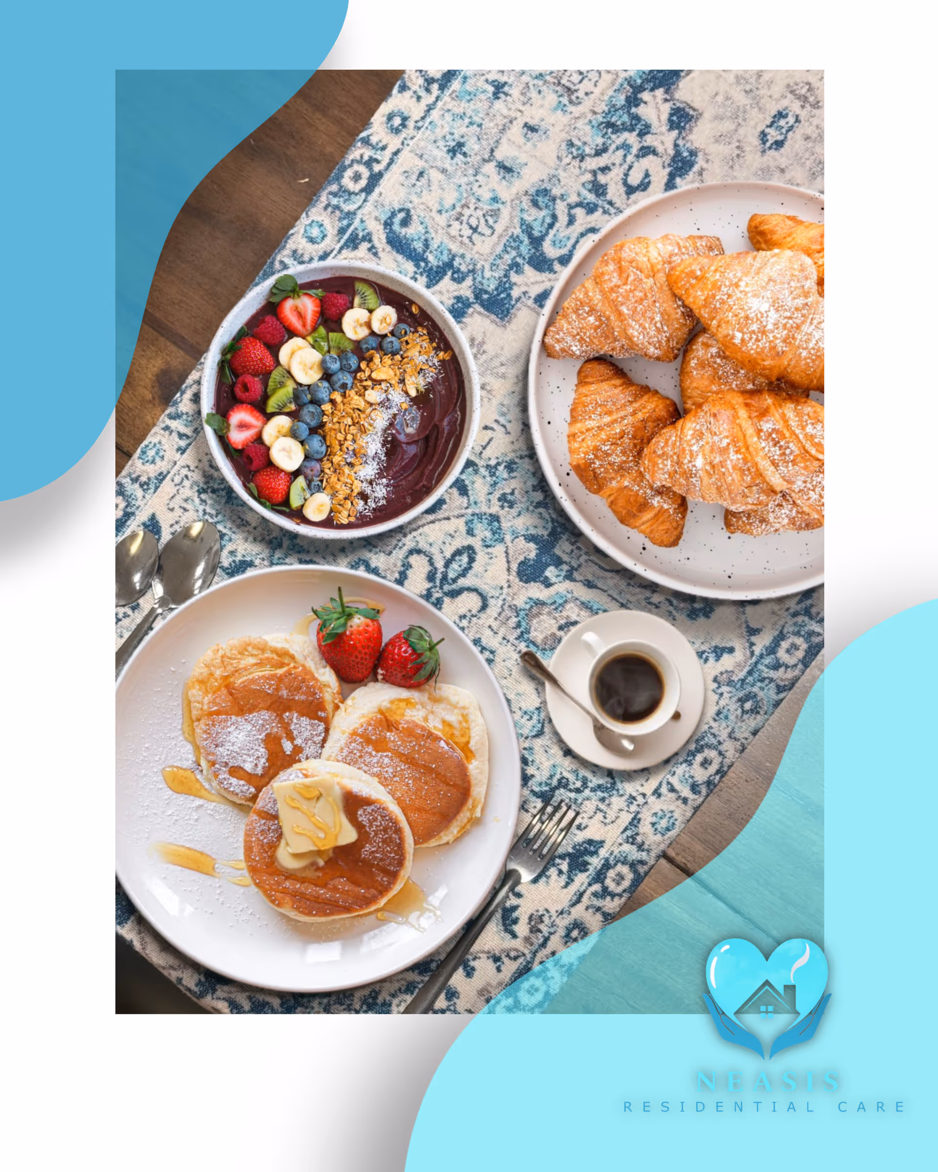 A breakfast spread on a patterned blue and white tablecloth featuring a plate of three pancakes topped with butter and syrup, two strawberries on the side, a bowl of acai topped with sliced bananas, strawberries, kiwi, blueberries, granola, and coconut flakes, a plate of croissants dusted with powdered sugar, and a small cup of black coffee with a spoon.