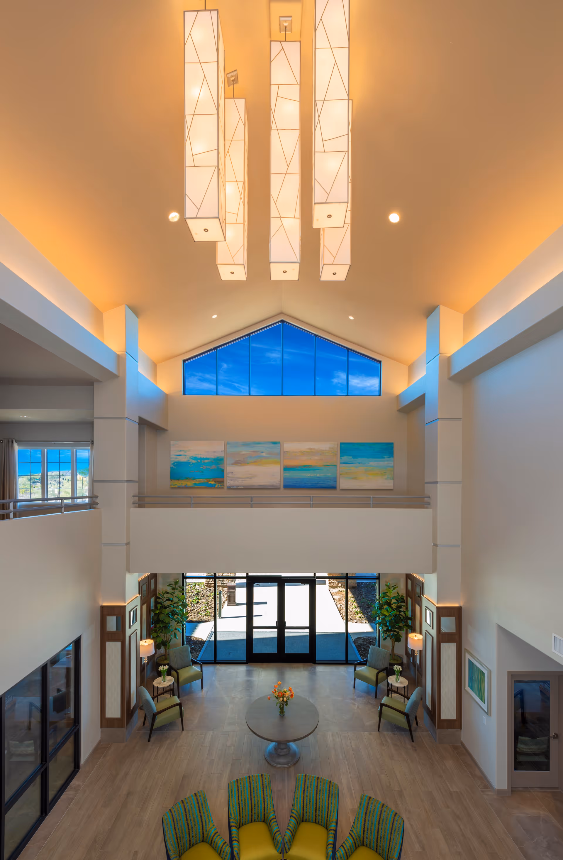 Spacious two-story assisted living lobby with a vaulted ceiling, modern hanging lights, seating areas and a large glass entrance.
