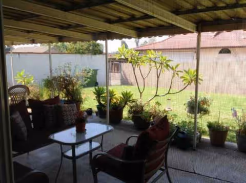 Covered outdoor patio with chairs, a table, and potted plants overlooking a grassy yard.
