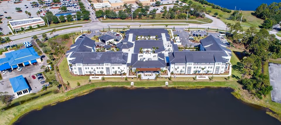 Aerial view of a U-shaped senior living facility complex along a lakeshore with parking and nearby roads.