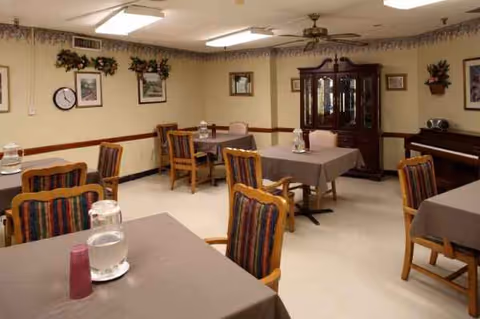 A dining room with several tables covered by gray tablecloths and striped chairs.