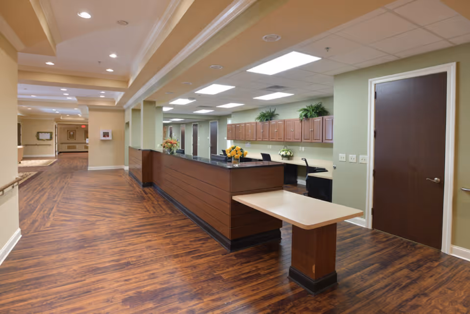 Well-lit reception area and hallway with a long wooden front desk, wood flooring, overhead lighting, and cabinets along the wall.