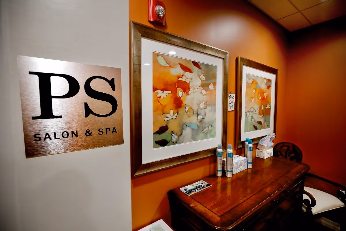Interior salon and spa area with framed artwork, a wooden table holding toiletries, and a sign reading "PS Salon & Spa".