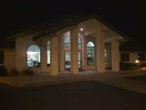 Night exterior of Lindsay Gardens Nursing & Rehabilitation entrance with arched windows and columns.