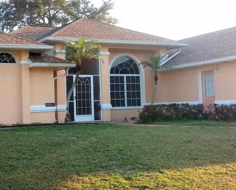 Front exterior of peach-colored assisted living facility with arched window and palm trees.
