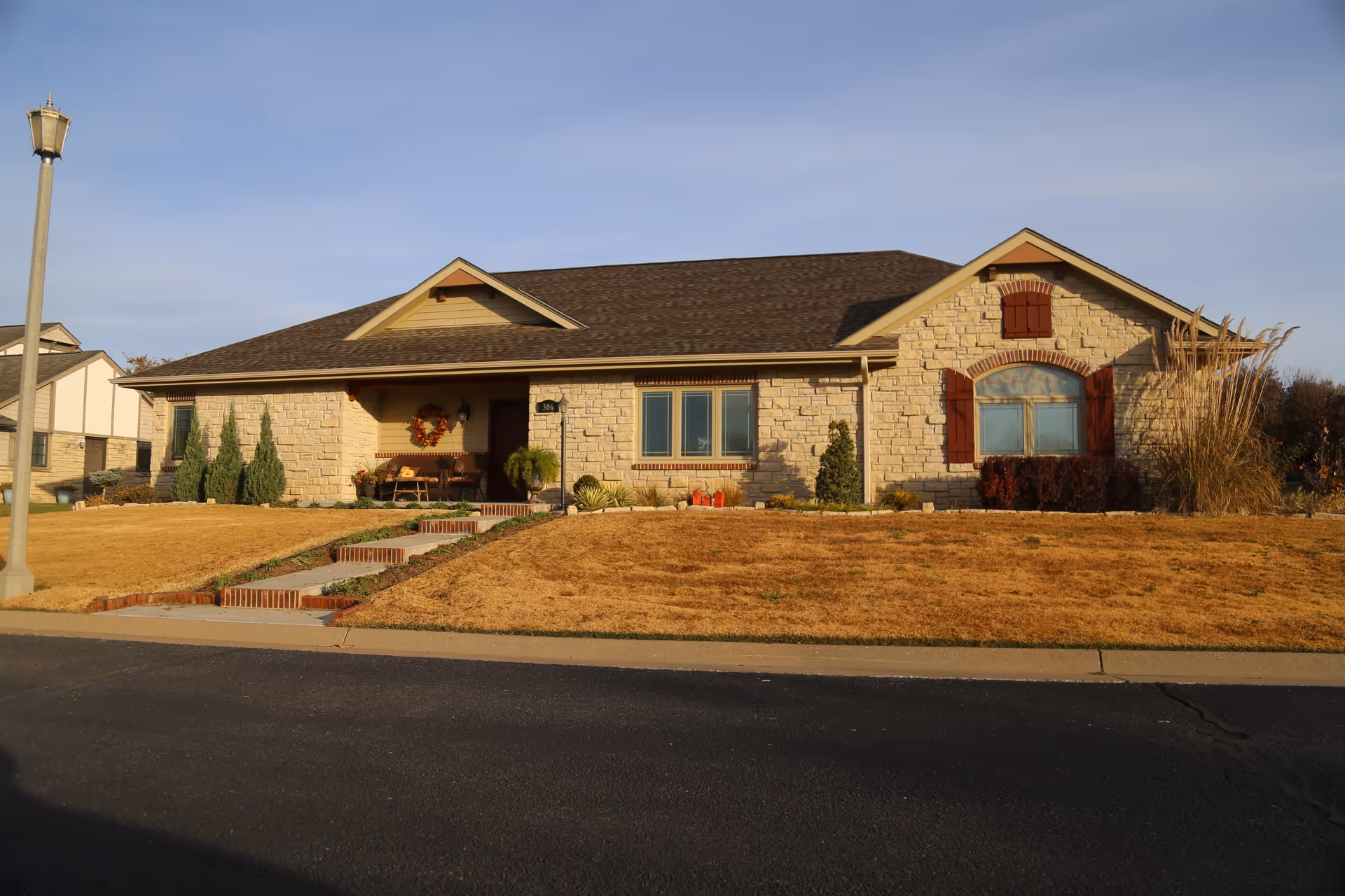 Single-story stone-faced ranch-style building with a front porch, windows with shutters, and a dry front lawn facing the street.