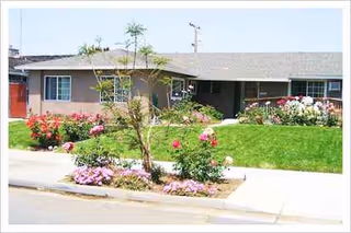 Single-story senior living facility facade with landscaped front yard and blooming flower beds.