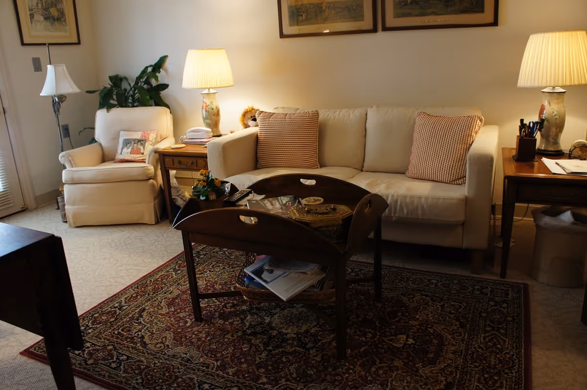 Cozy living room with a cream sofa and armchair, wooden coffee table on a patterned rug, and table lamps.