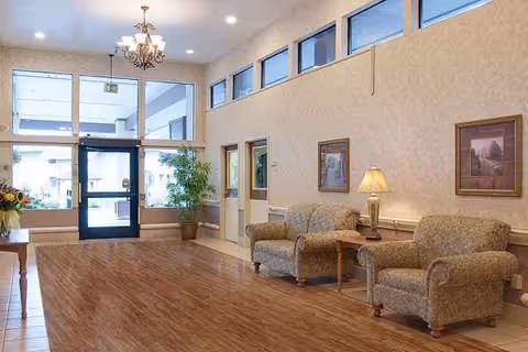 Spacious lobby area with beige seating, plants, lamps, and framed art near the entrance.