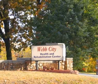 A sign for Webb City Health and Rehabilitation Center situated outdoors with trees and greenery in the background. The sign is mounted on a stone base with a grassy area in front.