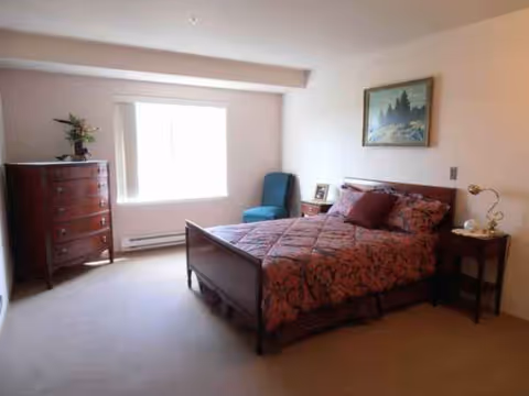 Bright bedroom with a wooden bed, dresser, nightstand, and a chair by the window.