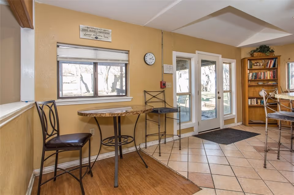 Small common area with a round table and chairs, a bookshelf, and double glass doors leading outside.