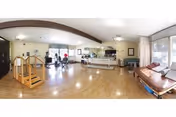Spacious senior living lounge with seating, a reception desk, and residents.