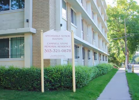 Exterior of Campbell Stone Memorial Residence senior housing with sidewalk and hedges.