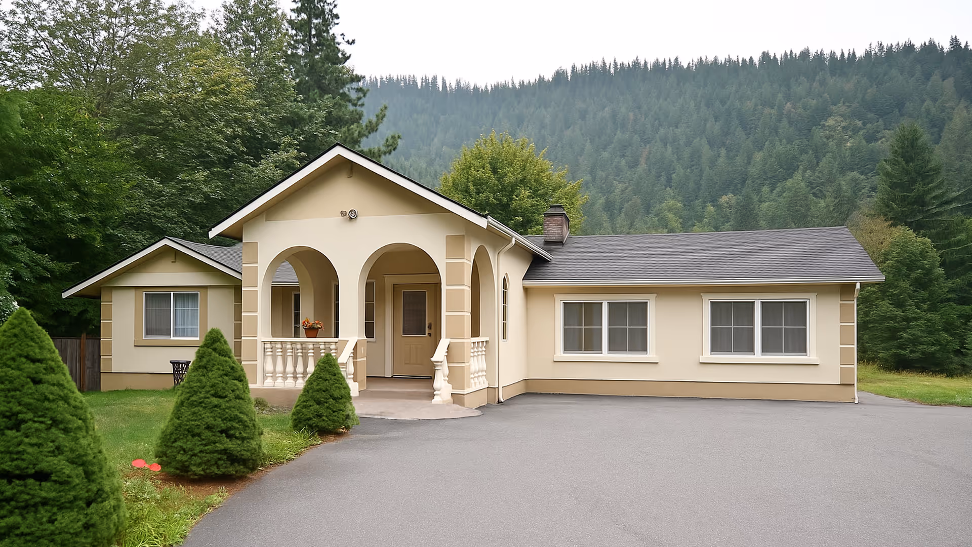 A single-story beige building with an arched front entrance and small porch, set in a green, wooded area.