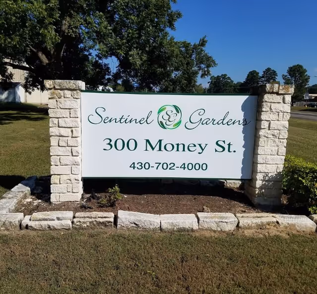 Outdoor entrance sign for Sentinel Gardens displaying the name, address 300 Money St., and a phone number.