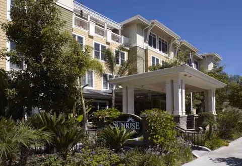 Exterior view of a multi-story senior living facility with a covered entrance and landscaping.