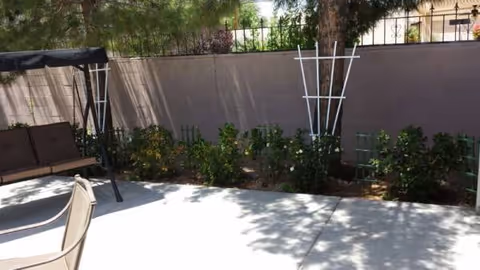 Outdoor patio with a swing bench, chairs, planters, and a beige wall.