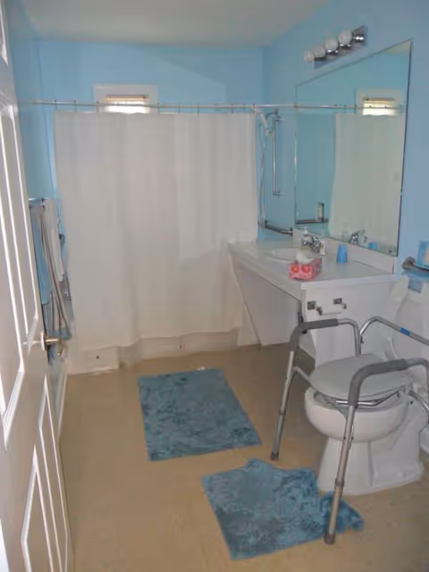 Senior living bathroom with blue walls, shower curtain, sink, mirror, and accessibility rails.