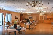 Spacious dining room with multiple set tables, chandeliers, wood flooring, and large windows along one wall.