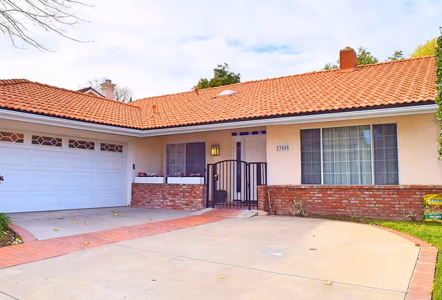 Single-story stucco house with a red tile roof, attached garage, gated front entry, and brick accents.
