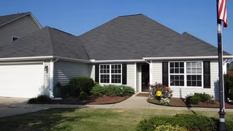 Single-story assisted living facility exterior with a front entrance, shrubs, and a flagpole