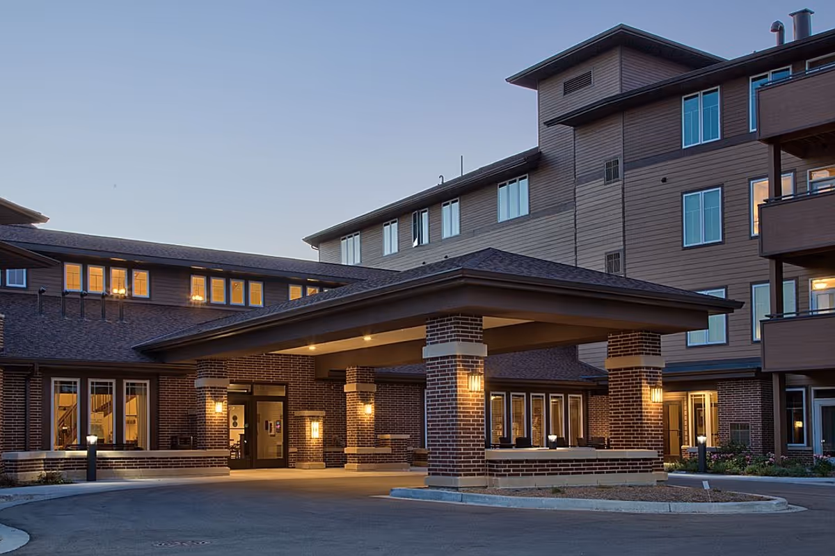 Covered entrance and porte-cochere of a multi-story residential building lit at dusk.