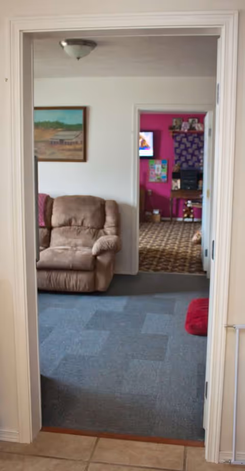 Doorway into a living area with a brown recliner and pink room beyond.