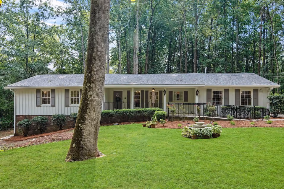 Single-story ranch-style building front with a wheelchair ramp, manicured green lawn, large tree, and wooded background.