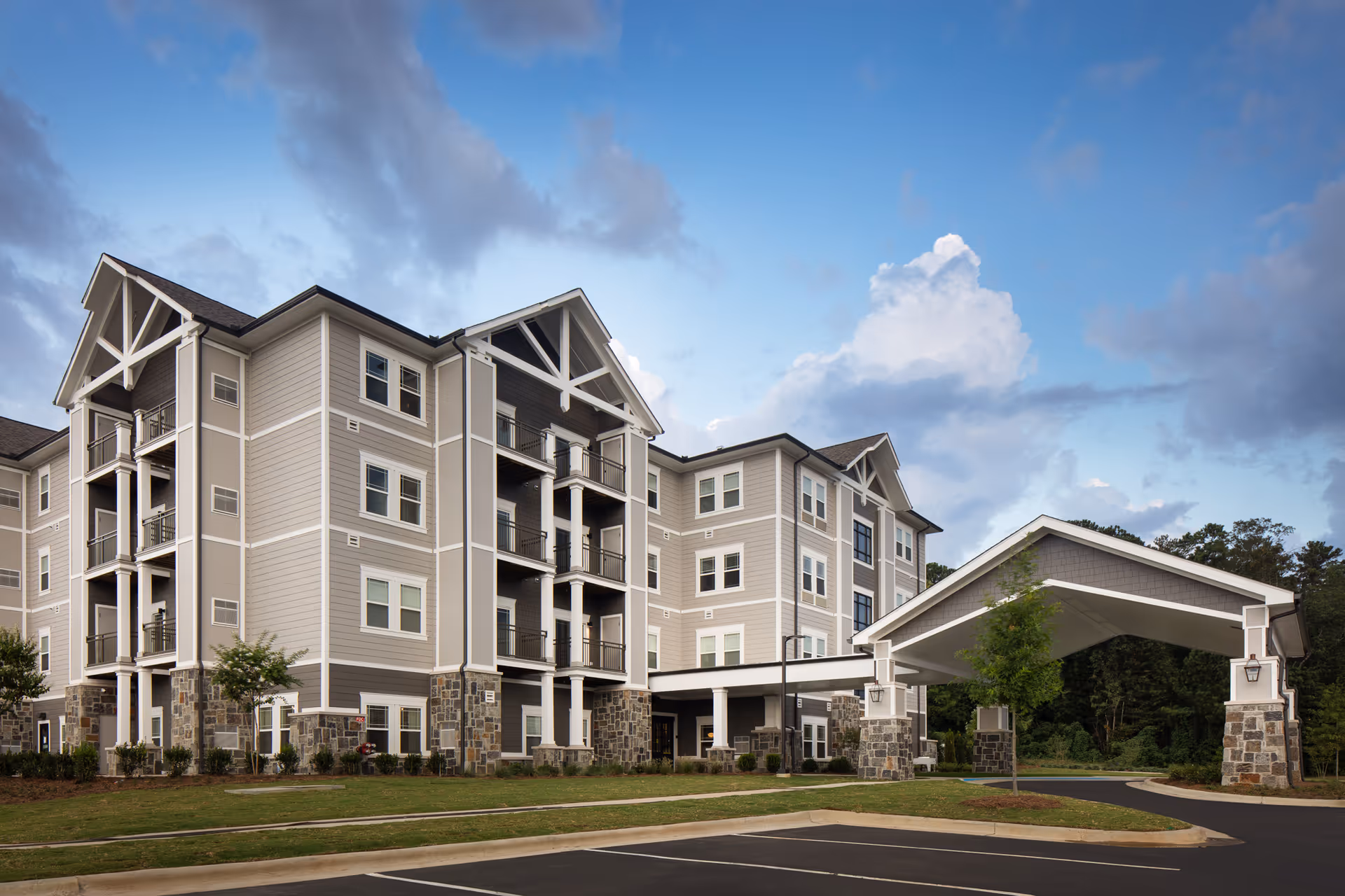 Exterior view of a four-story senior living building with balconies and a covered drop-off porte-cochere.