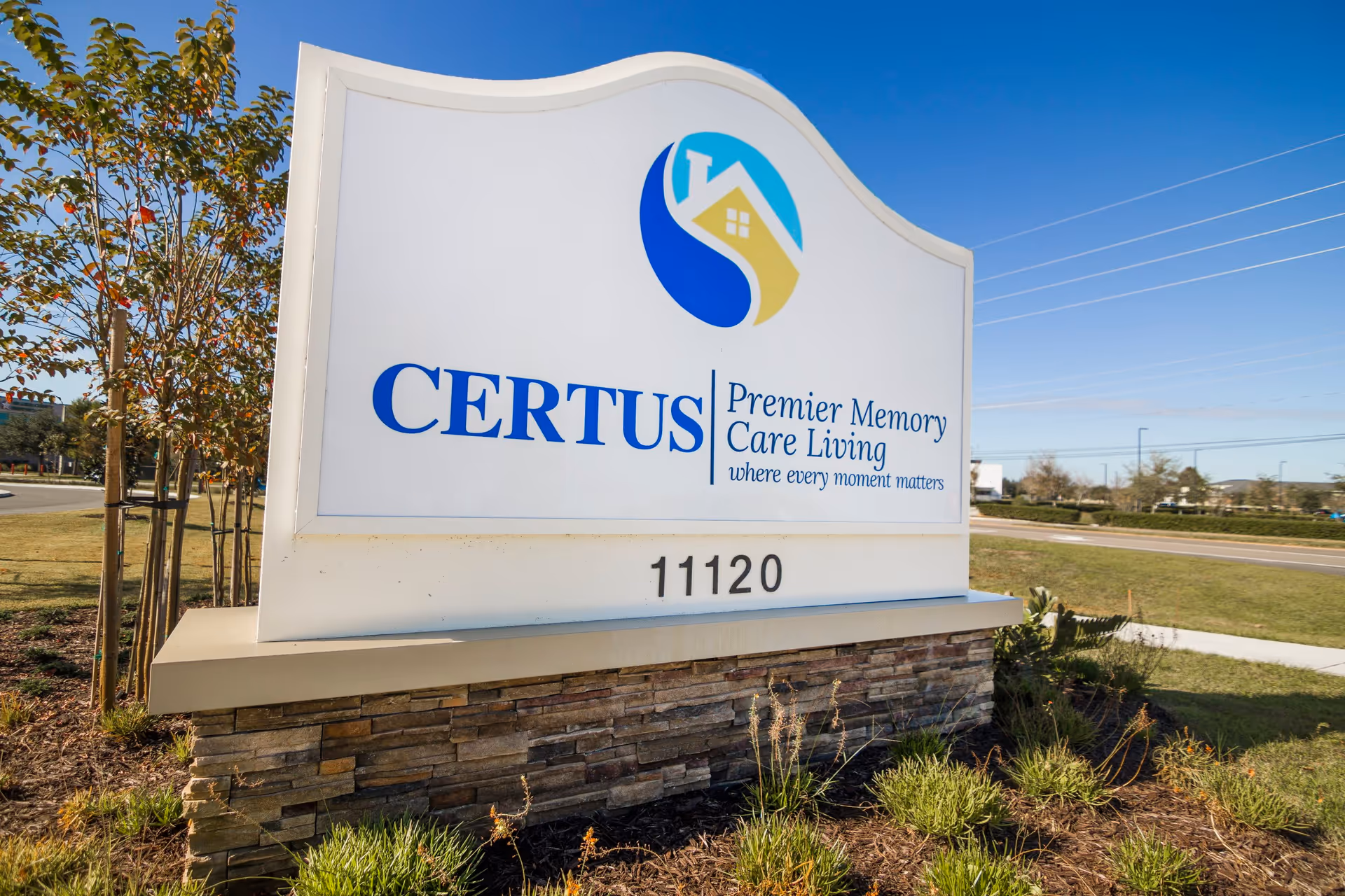 Outdoor sign for CERTUS Premier Memory Care Living with the tagline 'where every moment matters' and the address number 11120, set against a clear blue sky and landscaped greenery.