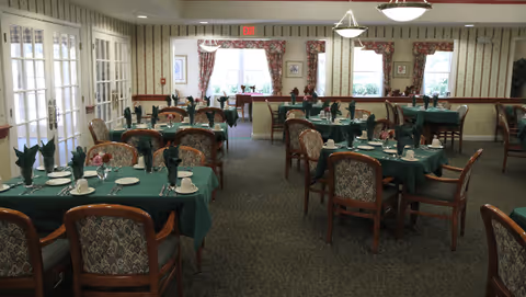 Dining room with multiple tables set with green tablecloths, folded napkins, and place settings.