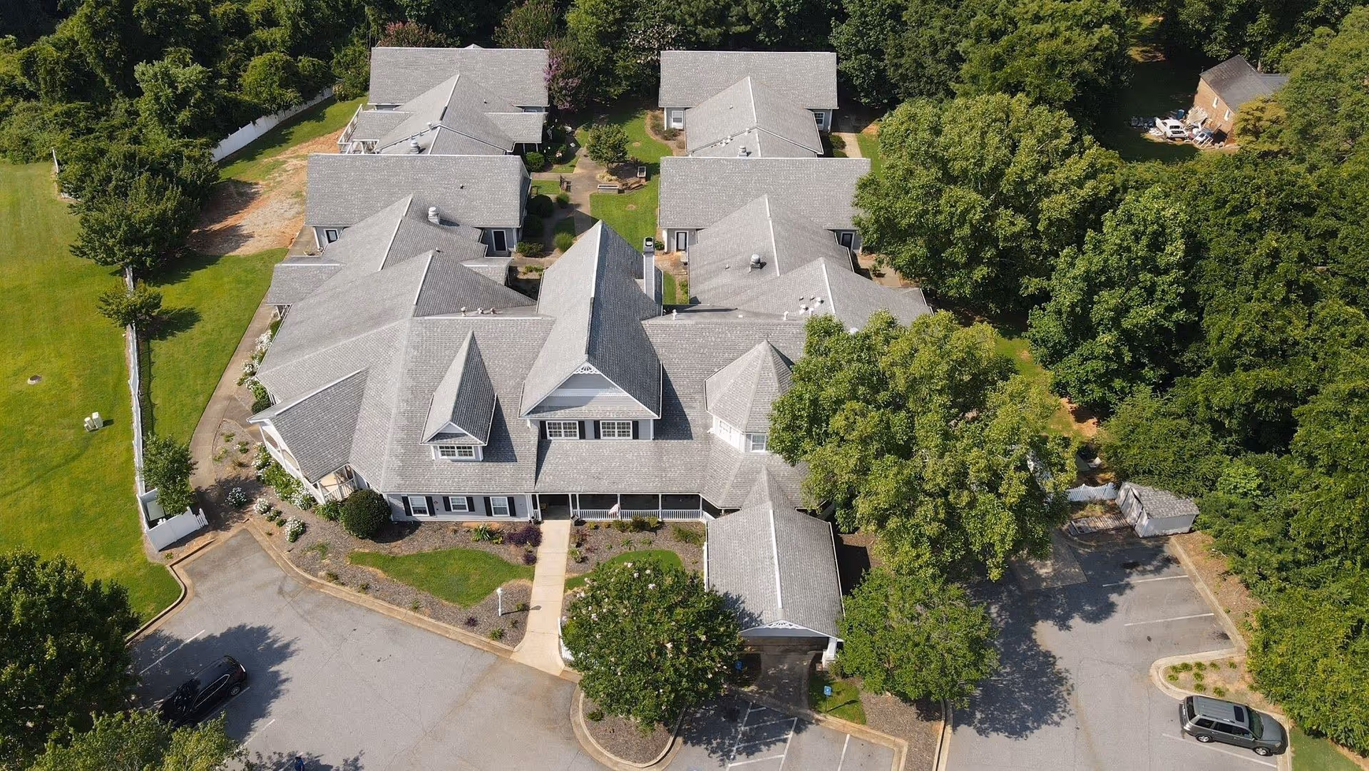Aerial view of Country Village Senior Living facility showing multiple connected buildings with gray roofs surrounded by green trees and lawns, with parking areas and walkways.