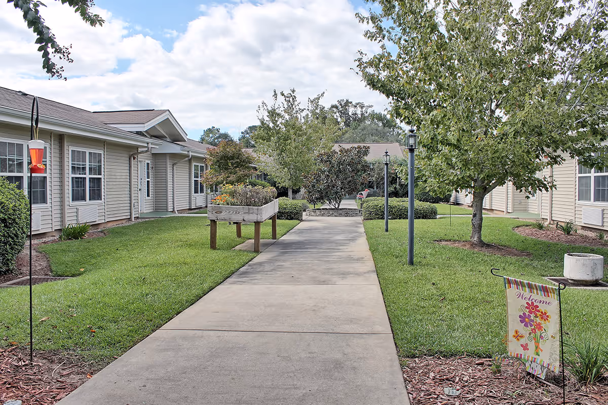 Exterior courtyard of Sodalis Quincy senior living, with walkway, lawns, trees, and welcome sign.