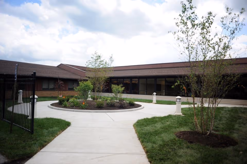 Circular paved courtyard with a planted center island and a low single-story building in the background under a cloudy sky.