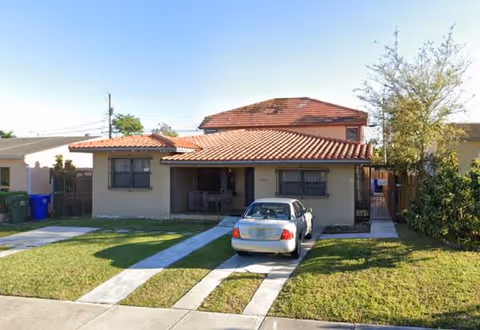 Front view of a single-story house with a red-tiled roof and a parked car.