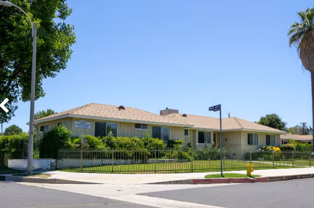 Exterior view of a single-story senior living facility with a lawn and street corner.