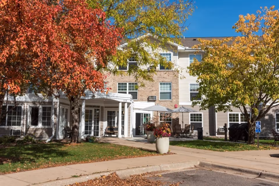 Exterior view of Briarcliff Apartments, a 55+ community, with autumn trees and patio seating.