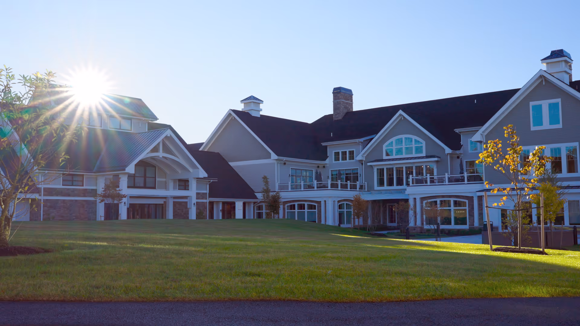 Large multi-story senior living building with a wide green lawn and the sunburst visible over the roof.