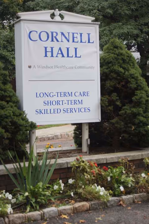 A large Cornell Hall sign sits among landscaping outside a care center.