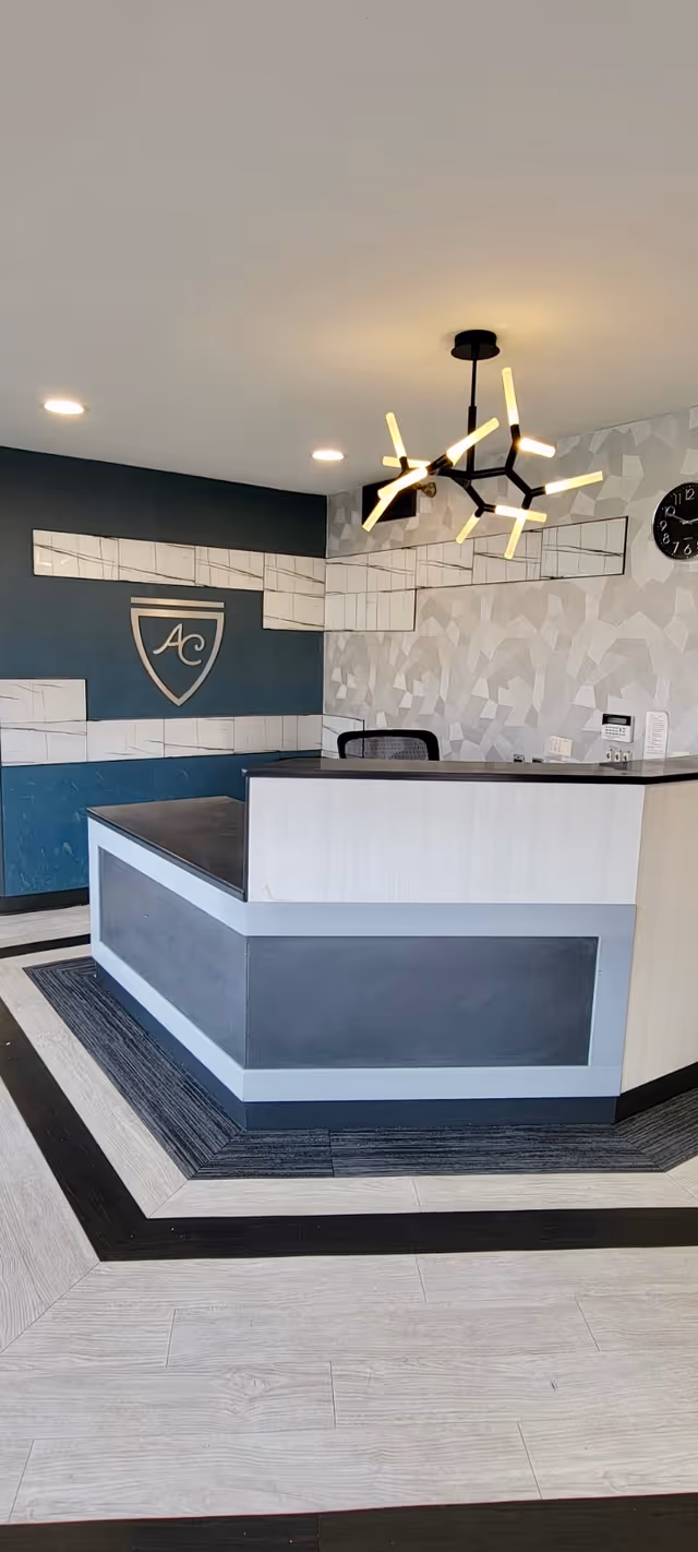 Modern reception desk and lobby area with geometric wallpaper, an 'AC' wall logo, and a contemporary chandelier.