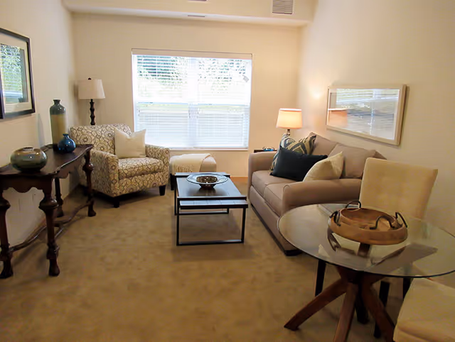 Furnished living room featuring a sofa, patterned armchair, coffee table, side tables, and a window with blinds.