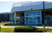 Front entrance of Hathaway Manor Extended Care showing a covered driveway with white columns, glass doors, and landscaped shrubs.