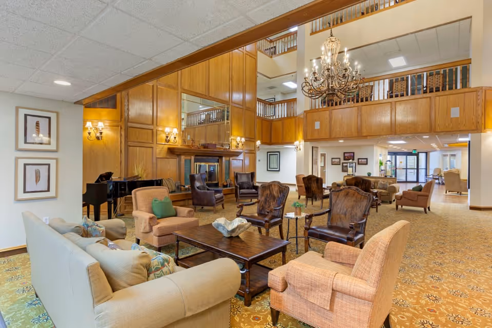 Spacious furnished common lounge with sofas, armchairs, a fireplace, piano, and chandelier.