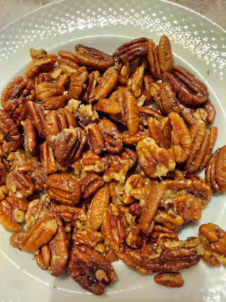 White plate piled with candied pecan halves.