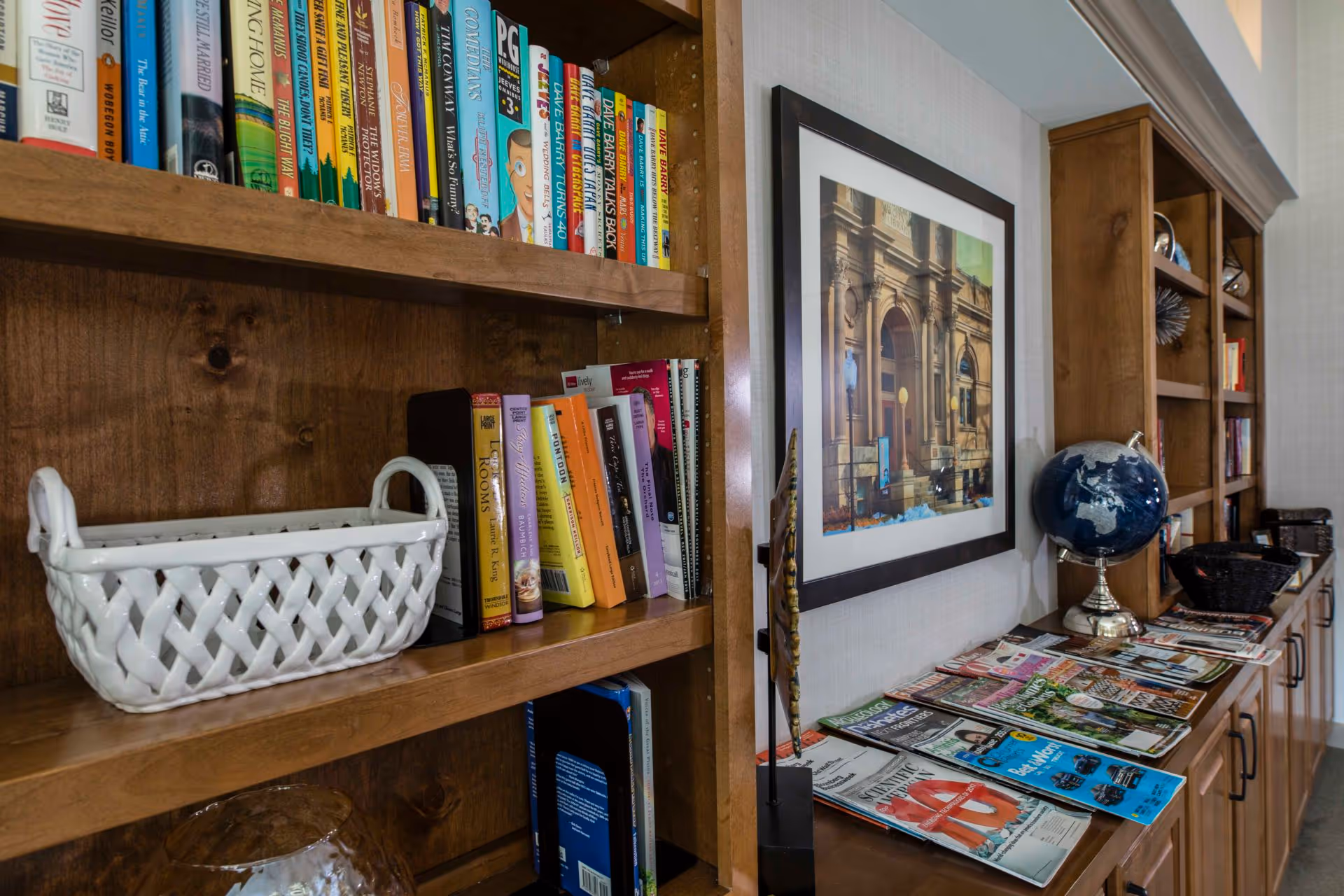 Wooden built-in bookshelves and cabinets filled with books, magazines, a globe, and framed artwork in a common area.