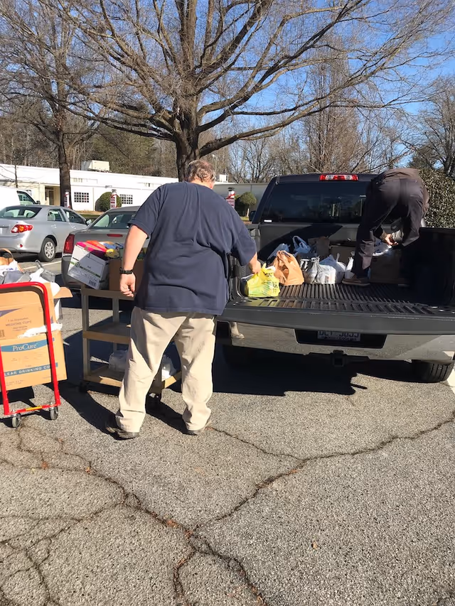 Two people load and unload bags and boxes from the open tailgate of a pickup truck in a parking lot.